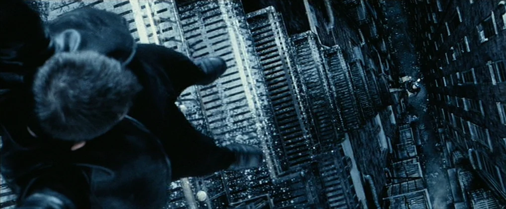 Minority Report movie still: closeup — A dark, dizzying view looking down from the edge of a high skyscraper. A man stands at the very edge, looking…
