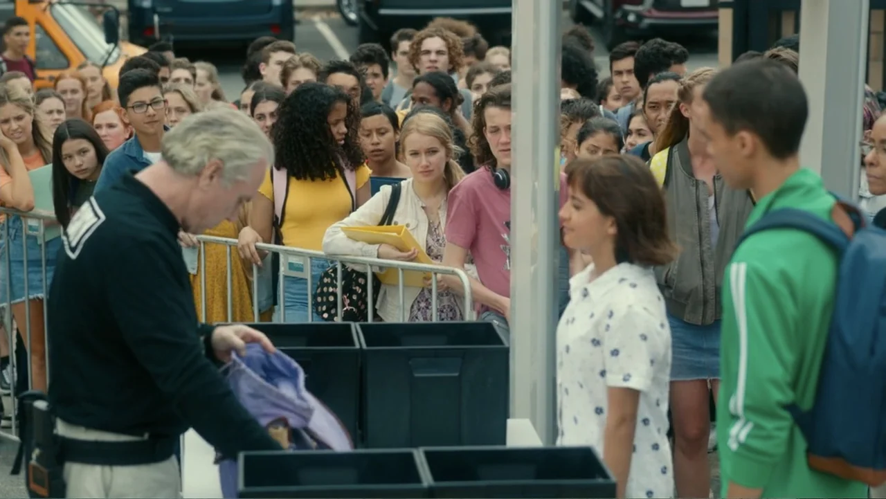 Dora and the Lost City of Gold (2019) movie still: medium — A group of students stands in a line behind a metal crowd control barrier. A man…