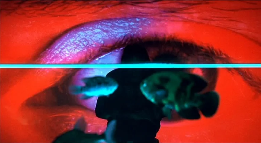 Gray’s Anatomy (1996) movie still: closeup — A close-up of a giant eye serves as the backdrop behind a dark silhouette. Several fish swim in the…