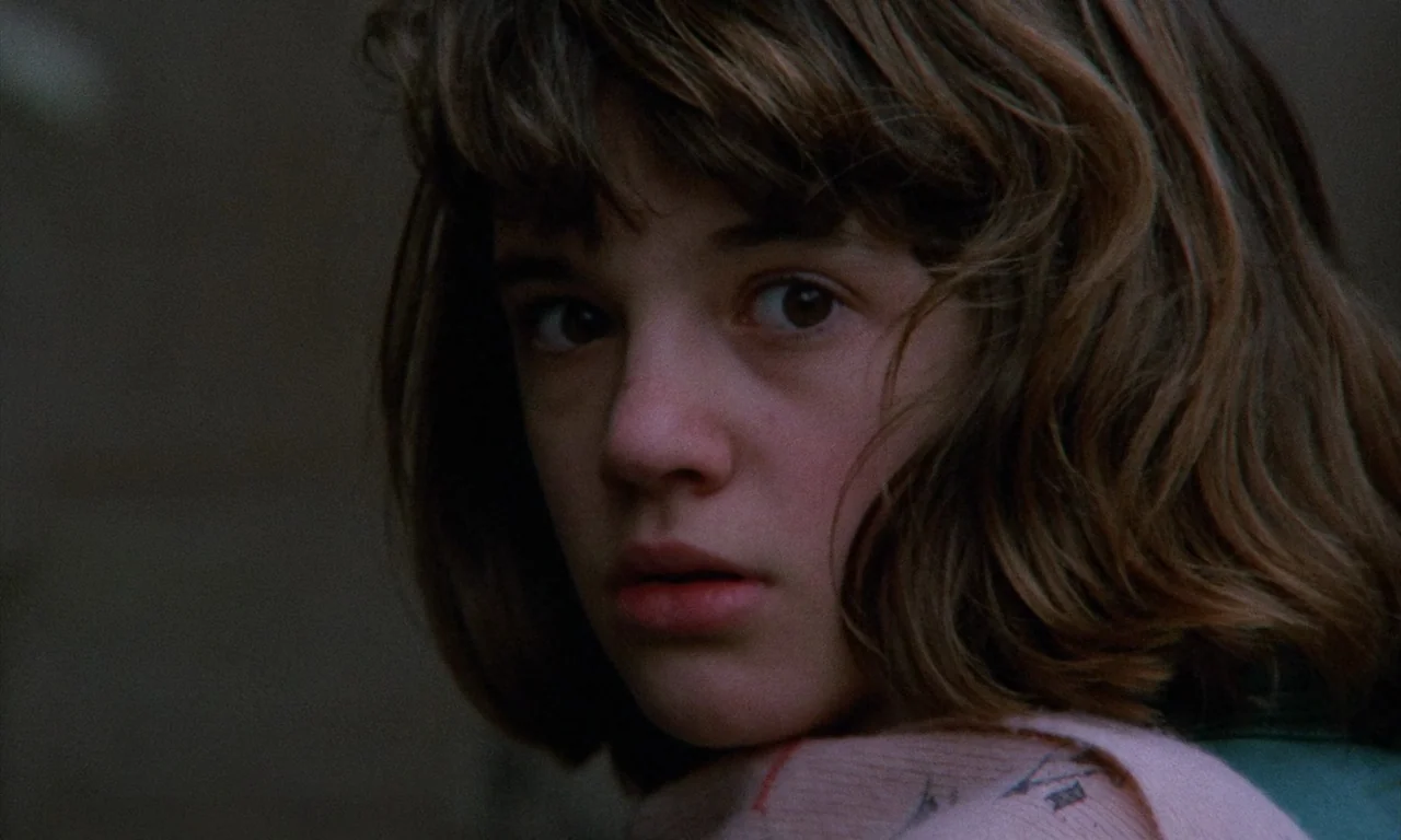 The Church (1989) movie still: closeup — A close-up shot focuses on a young woman outdoors against a blurry dark background. She turns her head to…