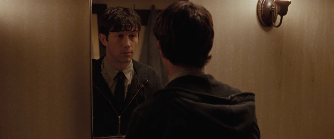 500 Days of Summer (2009) movie still: medium — A small residential bathroom with beige walls and a simple wall sconce. A young man stares at his…