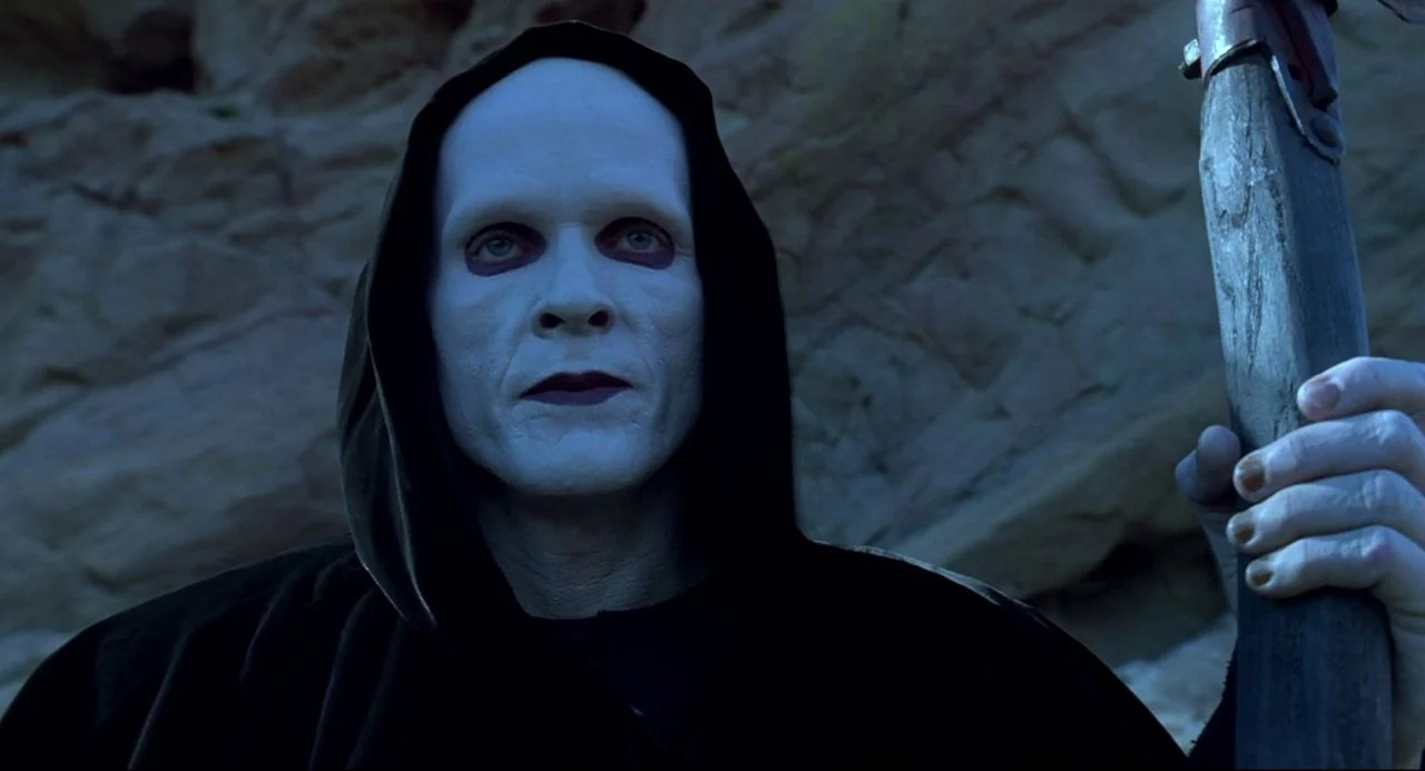 Bill and Ted’s Bogus Journey (1991) movie still: closeup — A figure stands in front of a textured, light-colored rocky cliffside outdoors. The…