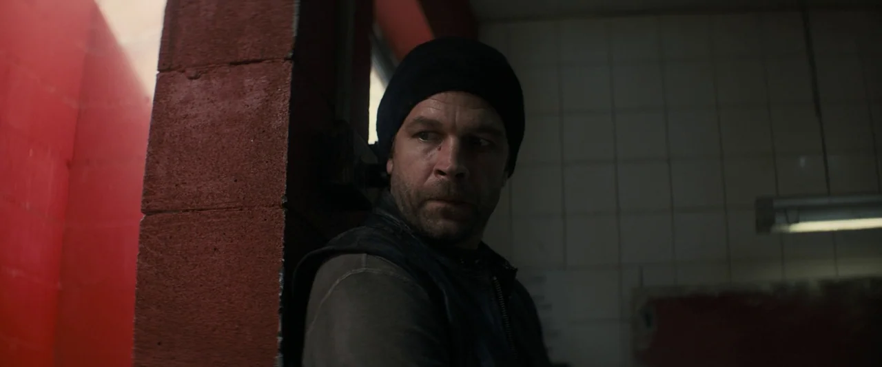 Don’t Breathe 2 (2021) movie still: medium — A dark, utilitarian space features white tiled walls and a bright red structural pillar. A man in a…