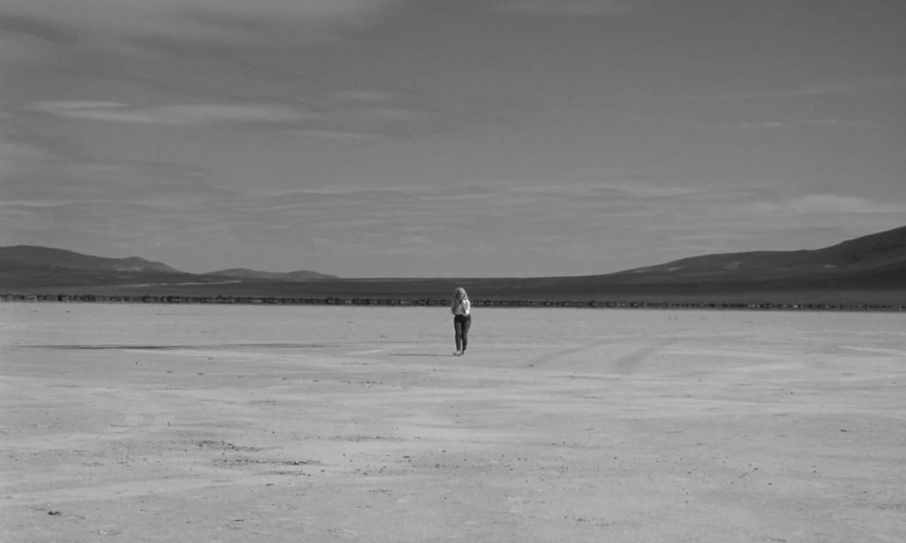 The Misfits (1961) movie still: wide — A vast, expansive salt flat stretches out toward distant dark mountains under a cloudy sky. A solitary woman…