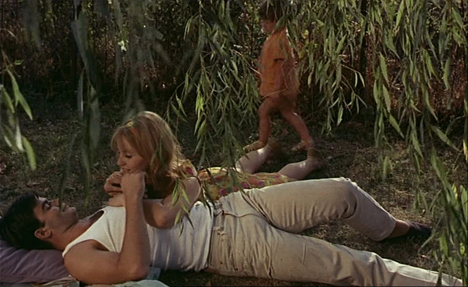 Le Bonheur (Happiness) (1965) movie still: medium — A man and a woman rest on grass beneath the sweeping branches of a willow. A small child in a…