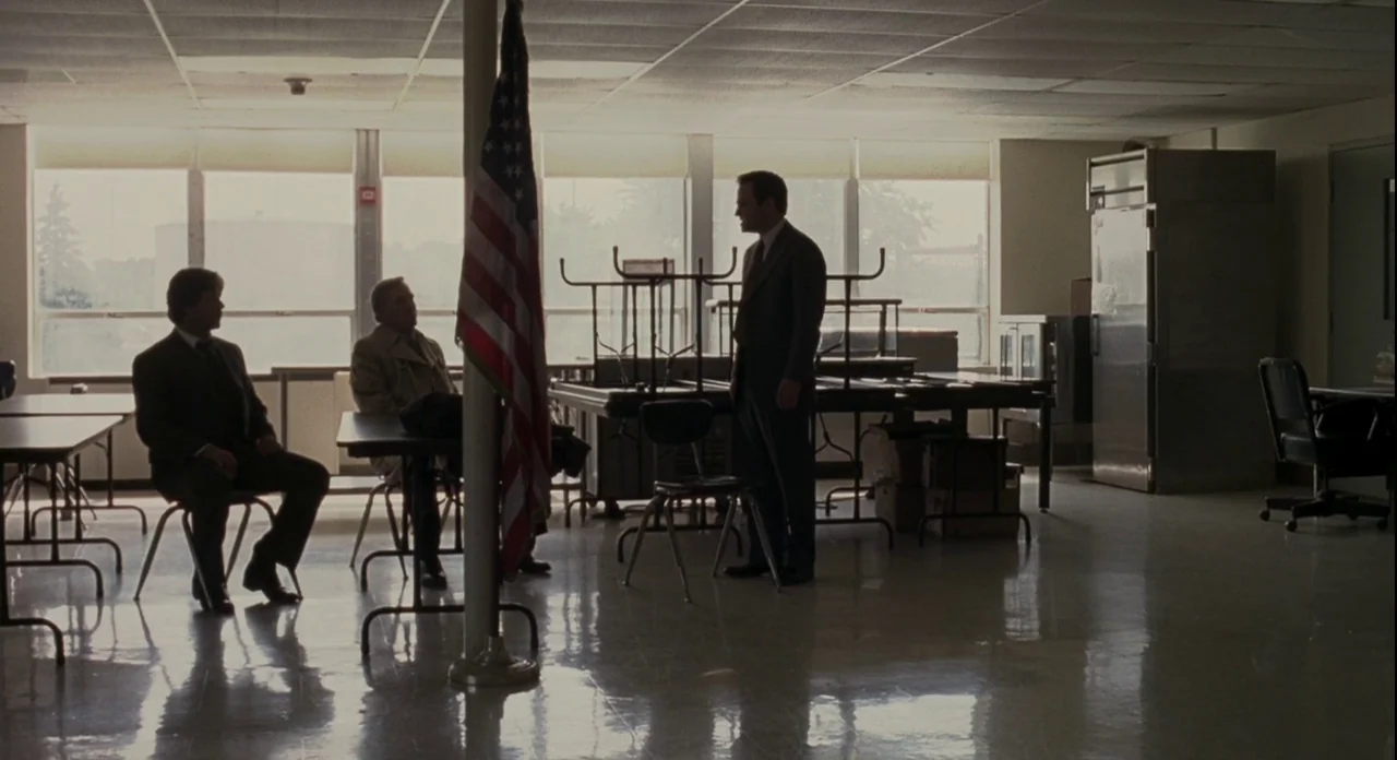 American Gangster (2007) movie still: wide — A sparse, institutional room features large windows and folding tables with metal legs. Three men in…