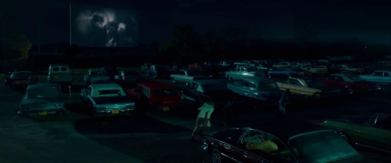 Scary Stories to Tell in the Dark (2019) movie still: wide — A drive-in theater at night features rows of vintage cars parked before a screen. A…