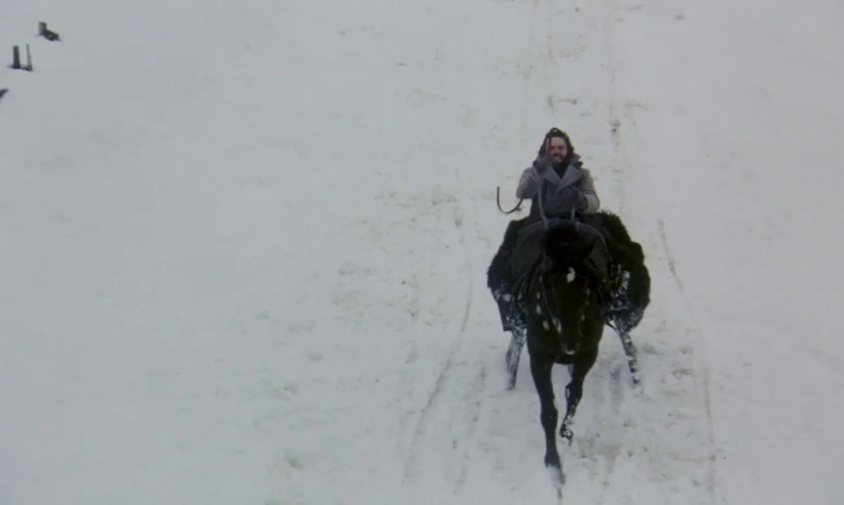 Kamouraska (1973) movie still: wide — A flat, snow-covered terrain stretches out under a grey, overcast sky. A man in a heavy coat drives a horse…