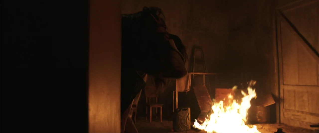 The Unholy (2022) movie still: medium — A dimly lit industrial room features a pile of debris and a wooden door. A person in a dark jacket stands…