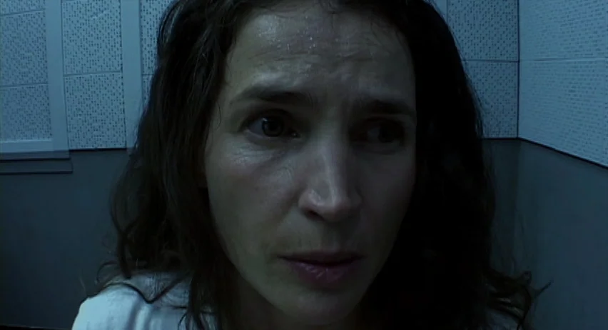 Inland Empire (2006) movie still: closeup — A corner of a room with light blue acoustic foam tiles on the wall. A woman with damp hair and skin…