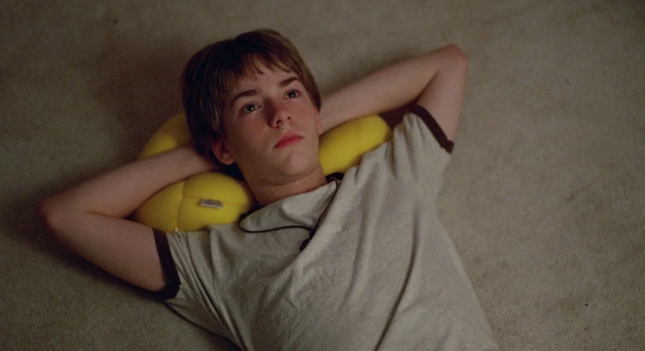Boyhood (2014) movie still: medium — A carpeted floor serves as the setting for a youth resting in a room. The boy lies flat on his back with his…