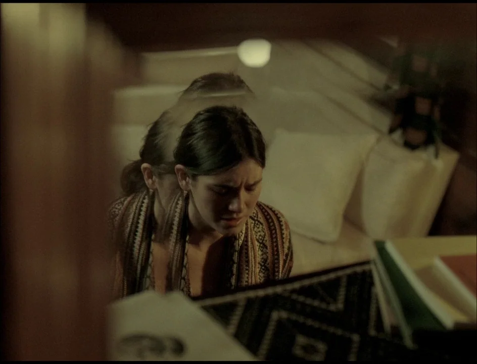Post Tenebras Lux (2012) movie still: medium — A dark, dimly lit room contains a person reflected in a glass surface. The subject sits with closed…