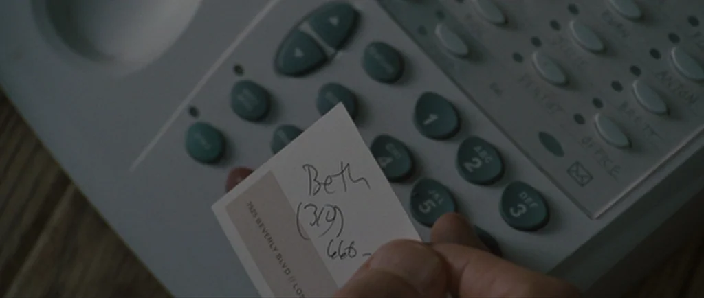 Greenberg (2010) movie still: closeup — A close-up view of an office telephone keypad and a person's hand. The person holds a small business card…