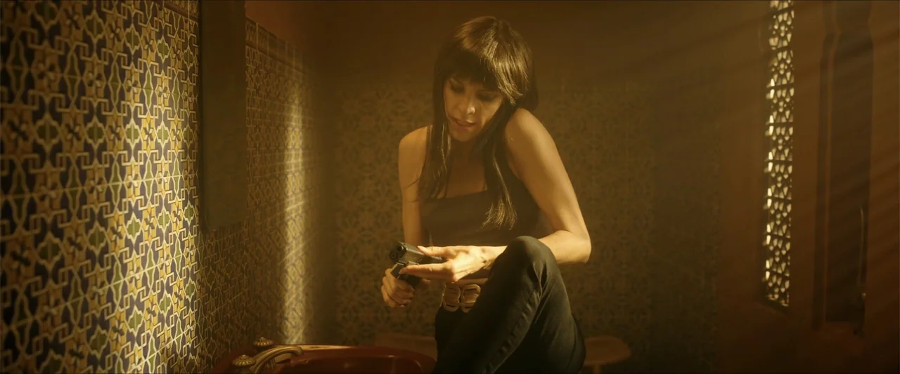 Checkmate (2015) movie still: medium — An interior bathroom features ornate geometric patterned tiles on the wall and a lattice window. A woman with…