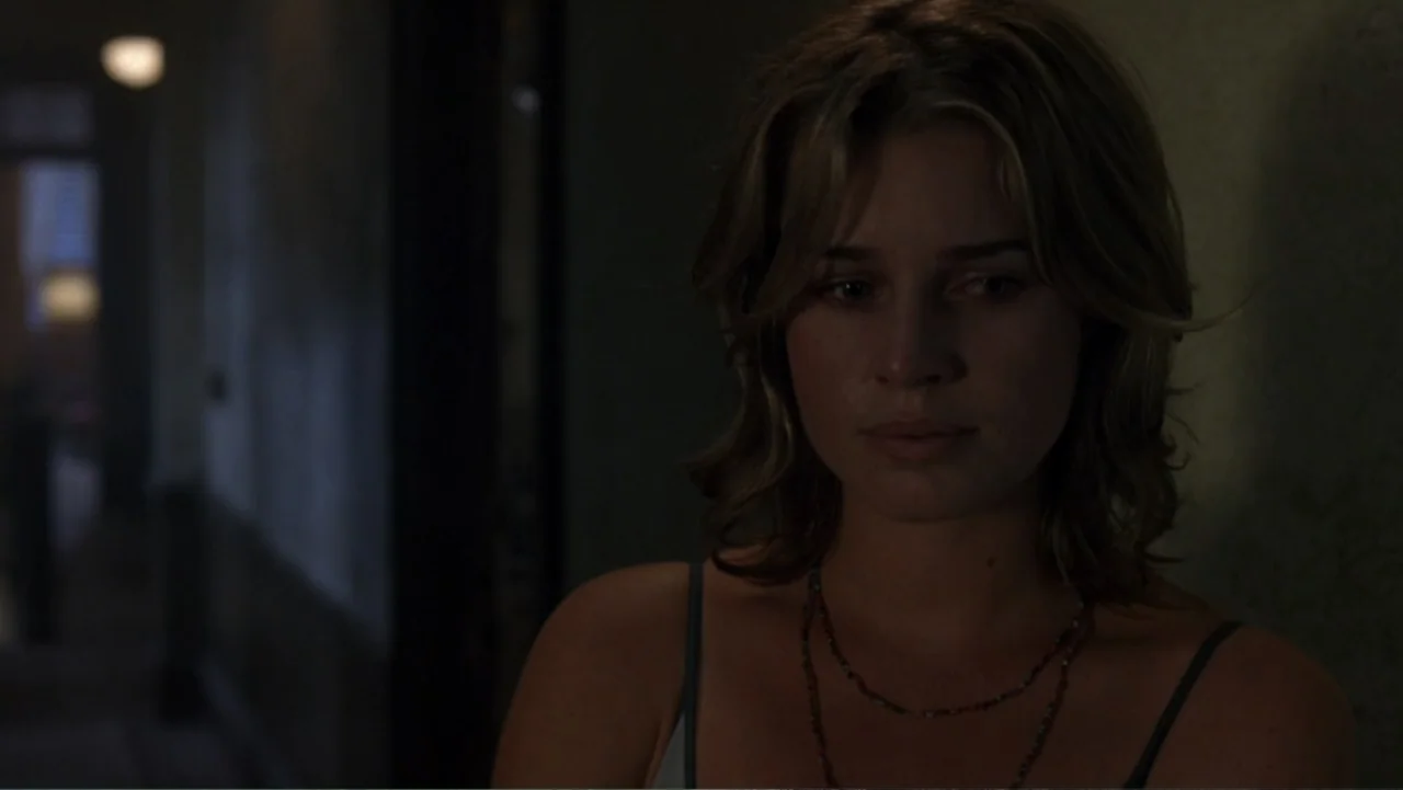The Punisher (2004) movie still: medium — A dimly lit interior hallway with blurred background architecture fading into darkness. A young woman in a…