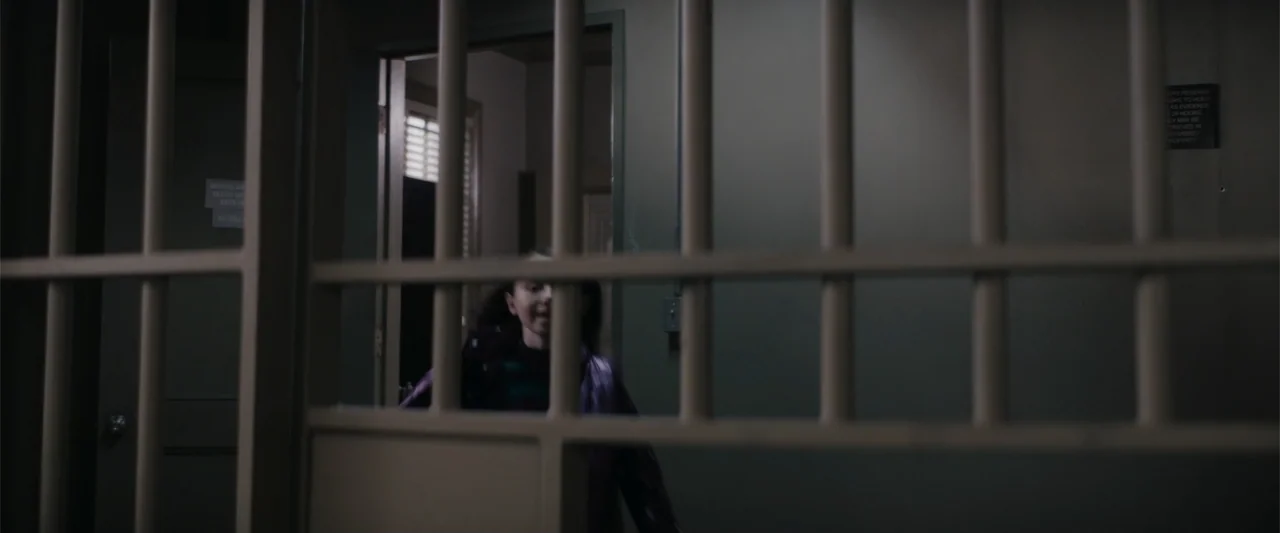 A Christmas Mystery (2022) movie still: medium — A dimly lit industrial hallway features metal barred gates and painted walls. A young girl moves…