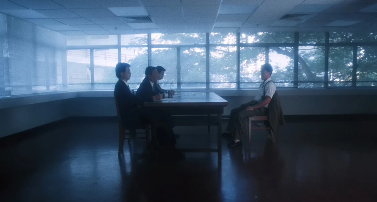 The Killer (1989) movie still: wide — A spartan room features a table with four chairs and large floor-to-ceiling windows. Three men in suits sit on…