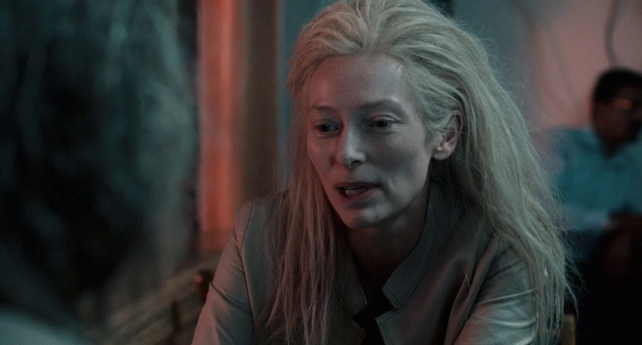 Only Lovers Left Alive (2013) movie still: closeup — A dimly lit restaurant or cafe booth features dark walls and ambient neon lighting. A pale…