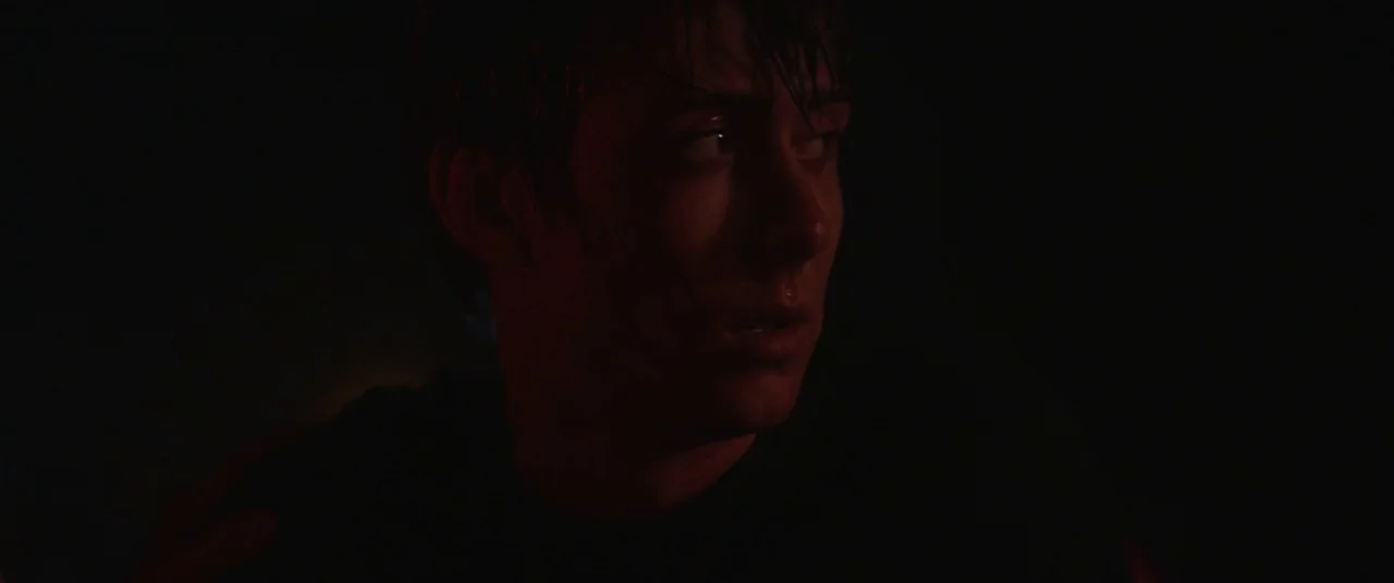 Super Dark Times (2017) movie still: closeup — A dark, dimly lit environment obscures the background details almost entirely. A young man with damp…