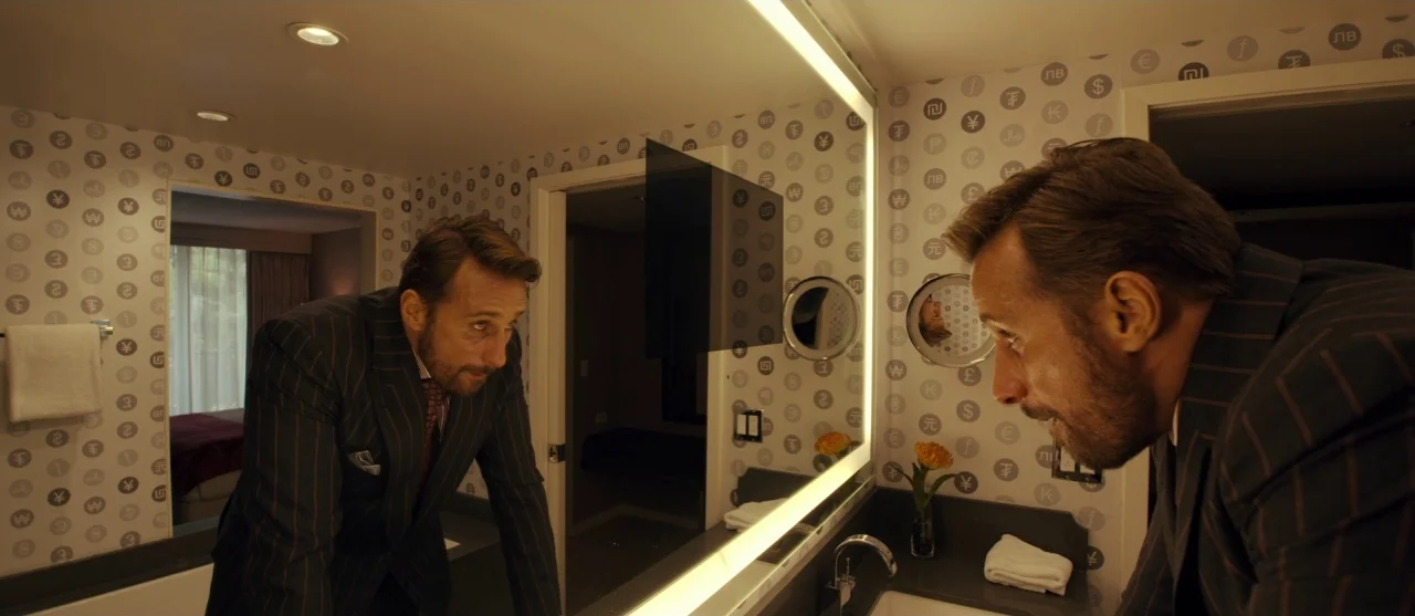 The Laundromat (2019) movie still: medium — A modern hotel bathroom features distinctive wallpaper patterned with various international currency…