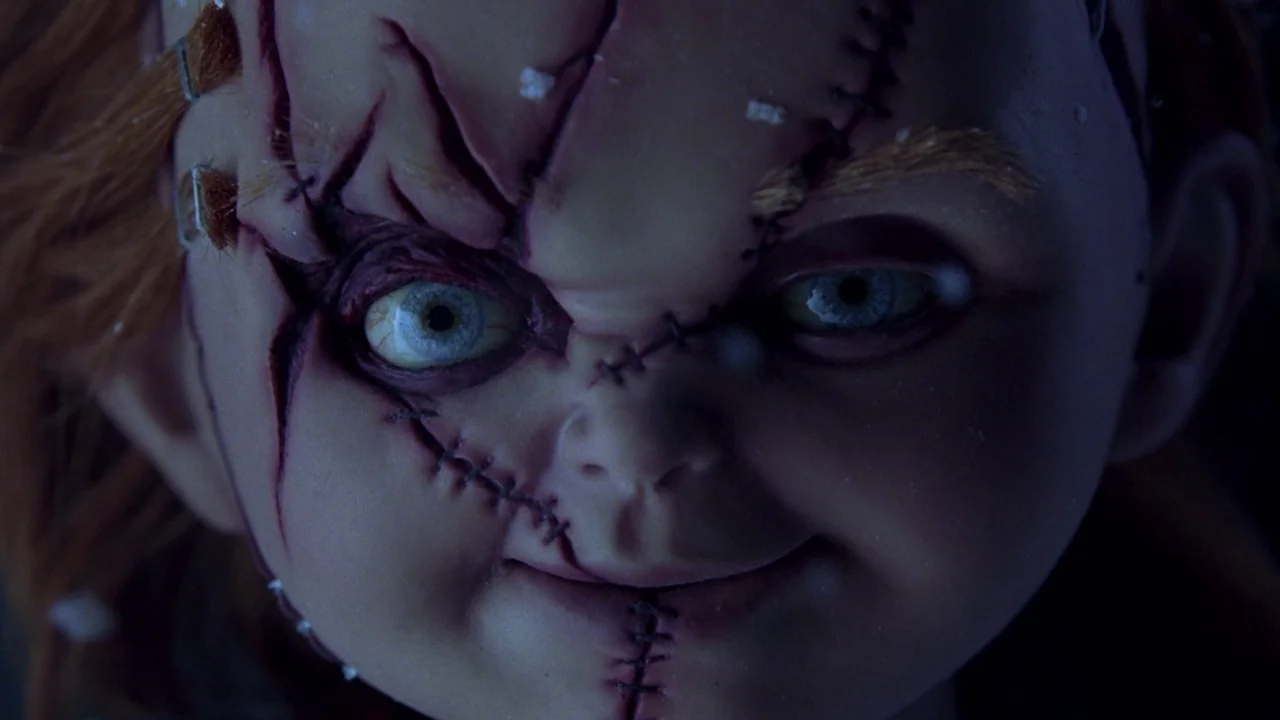 Seed of Chucky (2004) movie still: closeup — The face of a stitched-up doll fills the frame in extreme close-up. Deep shadows surround the character…
