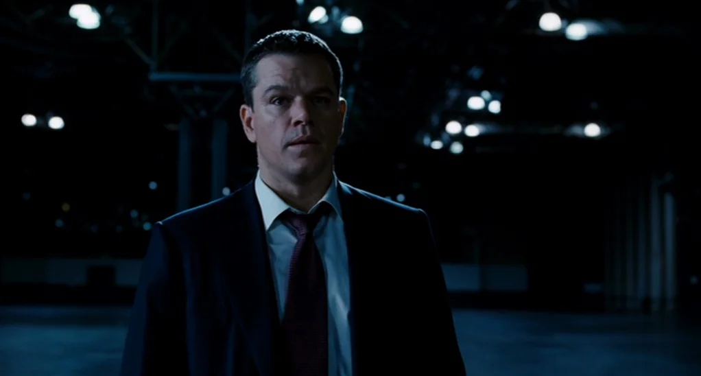The Adjustment Bureau (2013) movie still: medium — A vast, dark industrial space features blurred overhead lights in the deep background. A man…