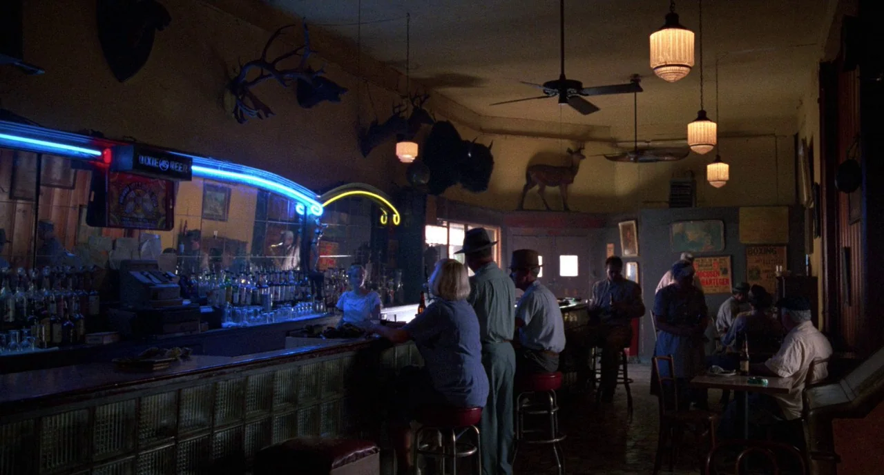 Angel Heart (1987) movie still: wide — A dimly lit 1940s establishment features a long wooden counter and taxidermy on walls. Multiple patrons sit…