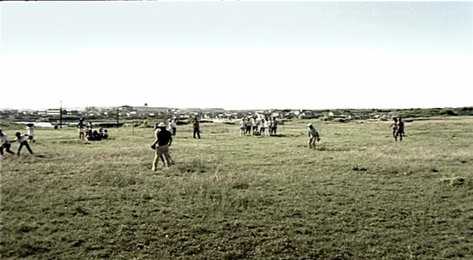 The Boys From Fengkuei (1983) movie still: wide — An open grassy field under a bright sky with scattered groups of people. Participants engage in…
