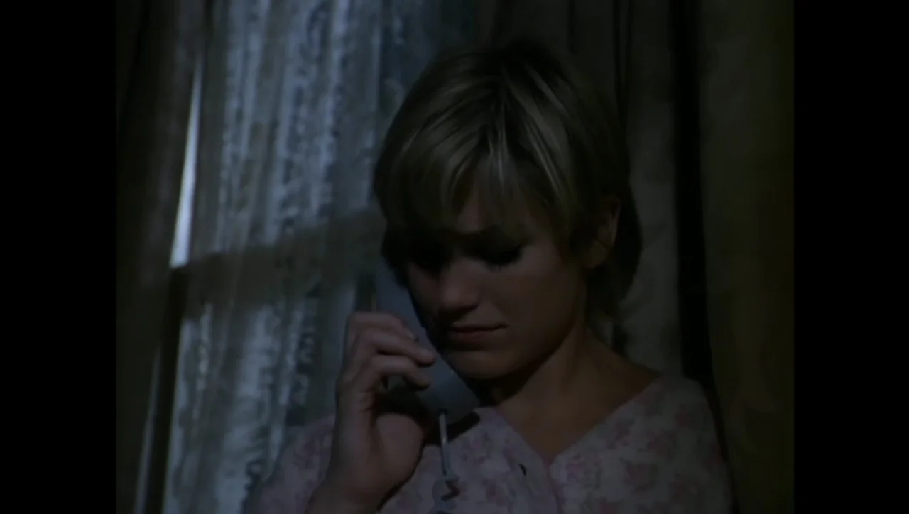 The Awakening (1995) movie still: closeup — A dimly lit interior room at night features a window covered by lace curtains. A young woman with short…