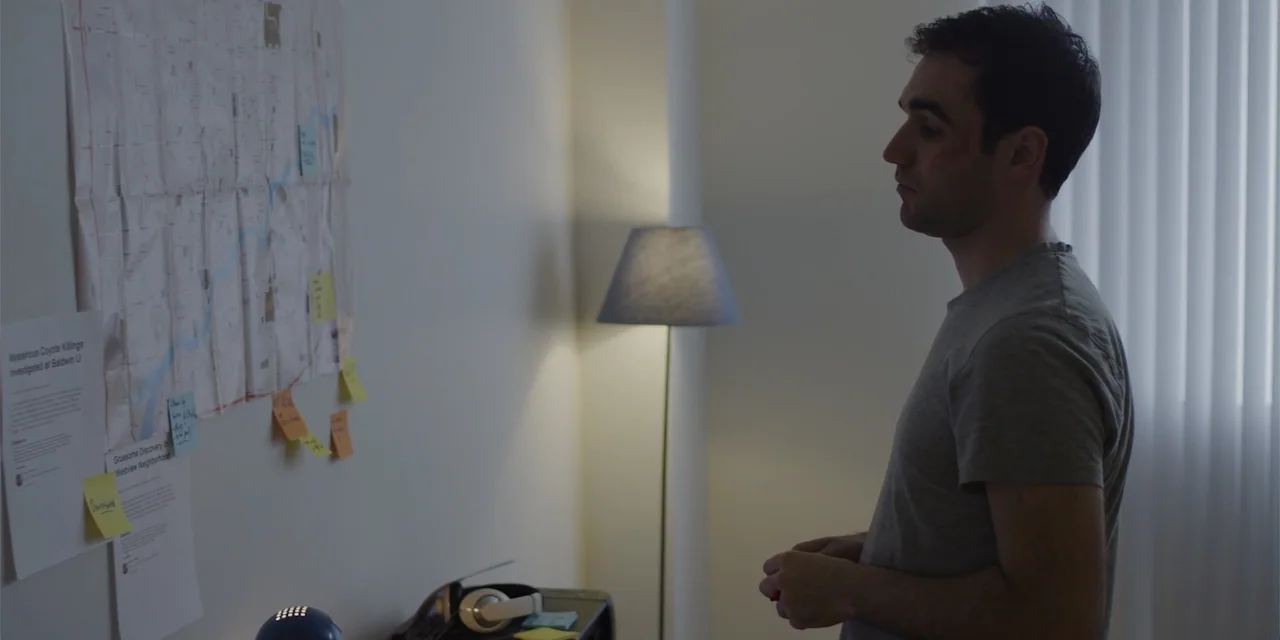 Lobos (2019) movie still: medium — A quiet home office features a wall covered in a large printed map with notes. A man stands in profile looking at…