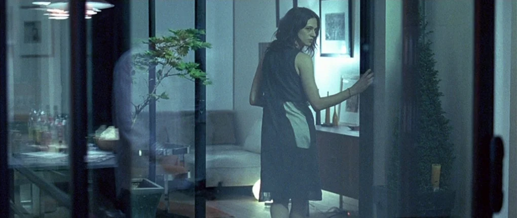 Boarding Gate (2007) movie still: medium — A modern apartment interior features glass room dividers, a console table, and potted greenery. A woman…