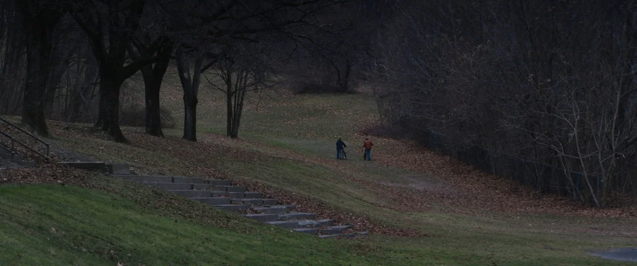 Super Dark Times (2017) movie still: wide — A park hill covered in autumn leaves features a concrete staircase on the left. Two figures walk away…