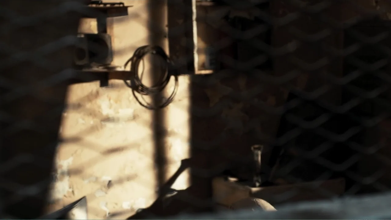 Gangs of Lagos (2023) movie still: establishing — A confined space features a weathered wall illuminated by bright, directional sunlight. A metal…