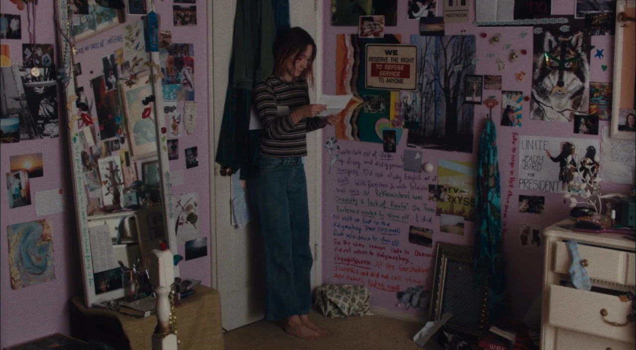 Lady Bird (2017) movie still: fullbody — A teenager stands in her room with pink walls covered in posters and handwritten text. She holds a letter…