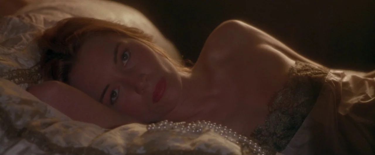 Dangerous Beauty (1998) movie still: closeup — A dimly lit interior with patterned pillows and soft textures. A young woman lies resting on her side…