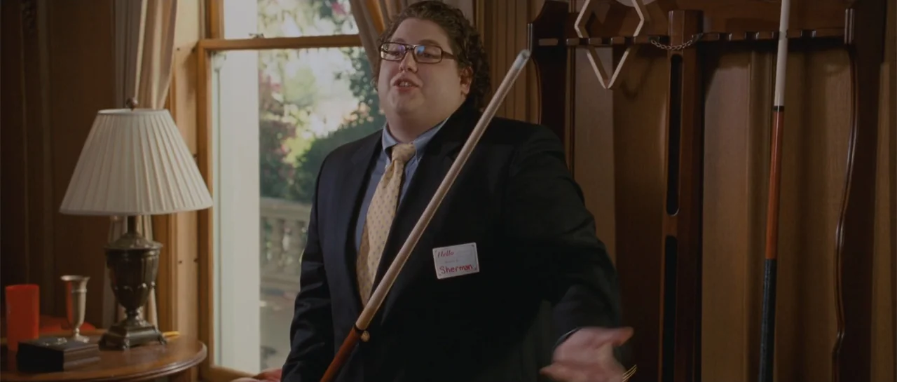 Accepted (2006) movie still: medium — A wood-paneled room interior features a large window with white curtains and blinds. A young man in a suit…