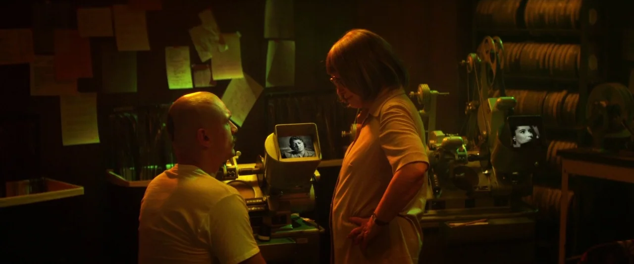 Zeroville (2019) movie still: medium — A dimly lit room contains film editing equipment and walls covered with posted notes. A bald man and a woman…