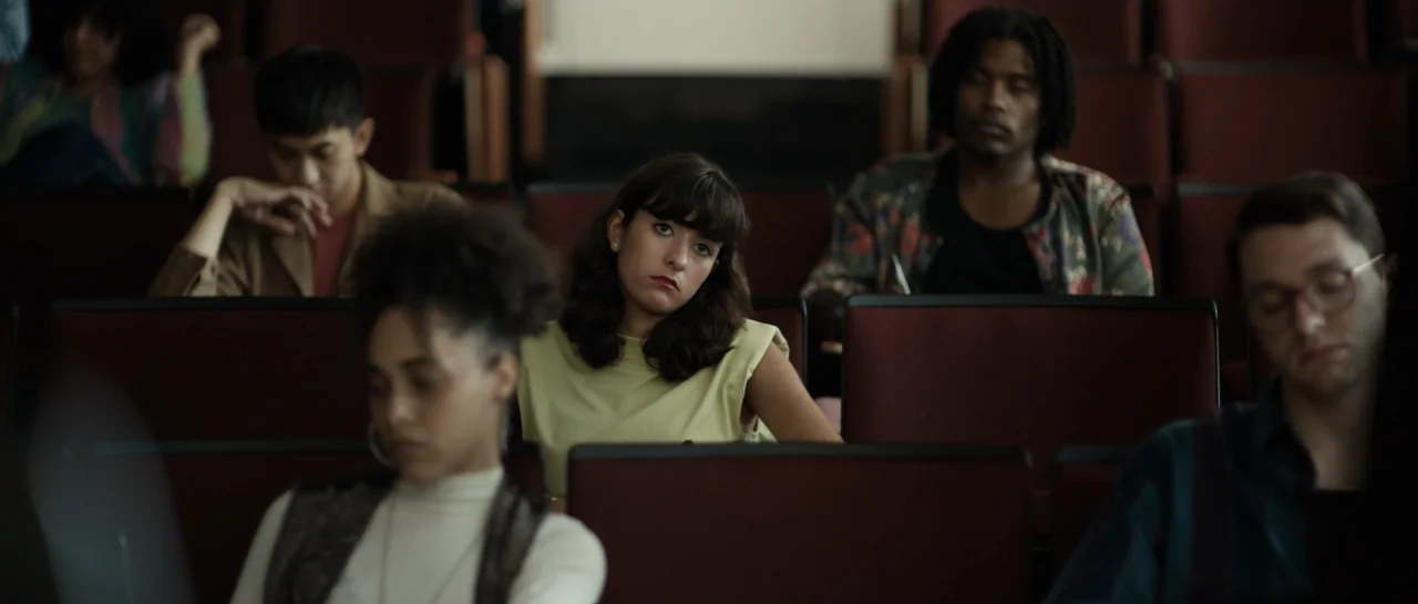 The Front Room (2024) movie still: medium — A rows of seating in a lecture hall with red upholstered chairs. Diverse students sit and observe a…