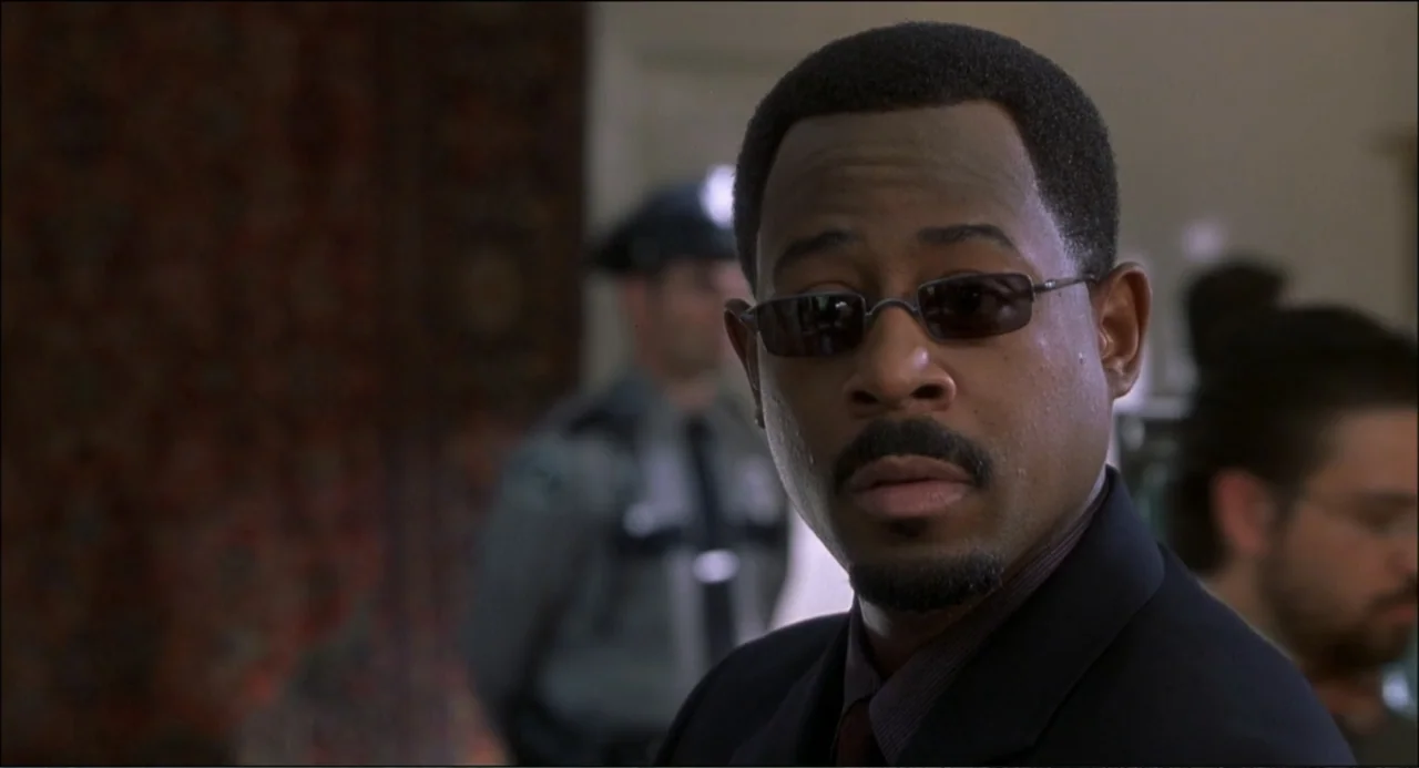 What's the Worst That Could Happen? (2001) movie still: closeup — A well-lit indoor office environment with blurred figures visible in the…