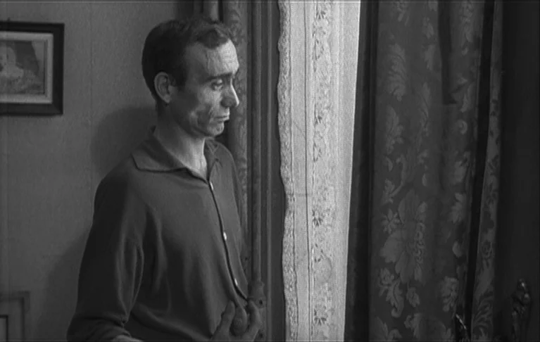 Le Signe du Lion (1962) movie still: medium — A 1960s residential interior features patterned curtains and a framed picture on the wall. A slender…