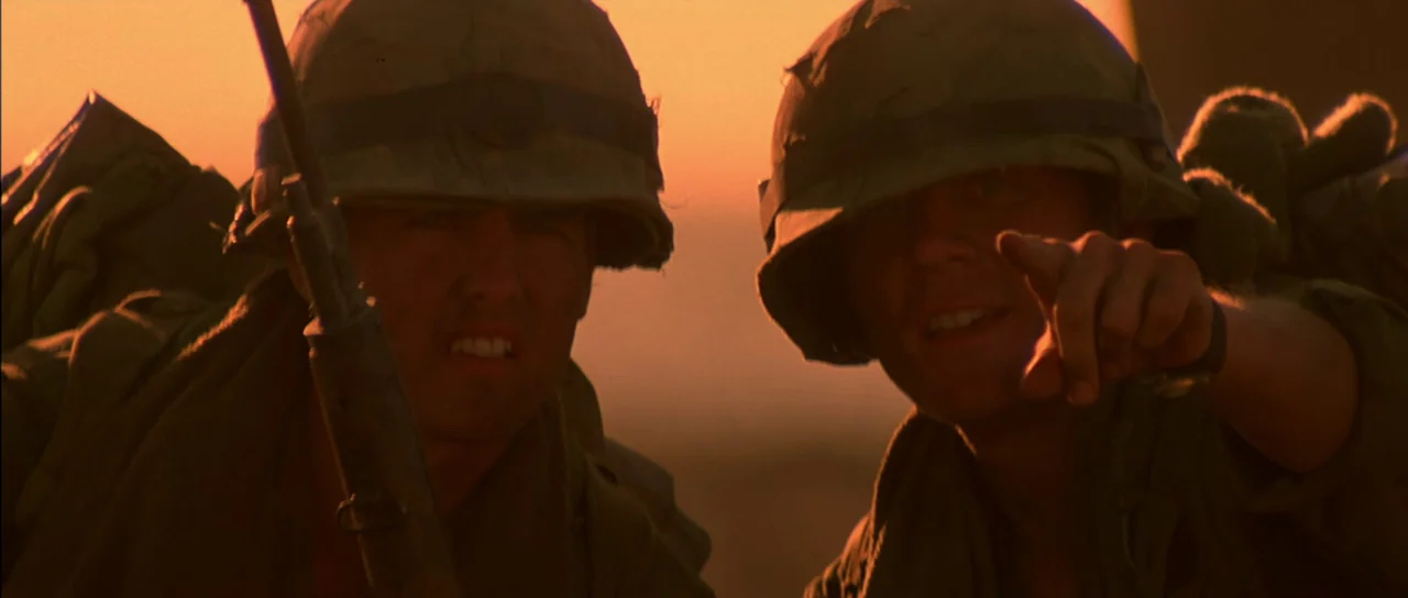 Born On The Fourth of July (1989) movie still: medium — Two soldiers in military helmets look toward an unseen target during a sunset. One soldier…