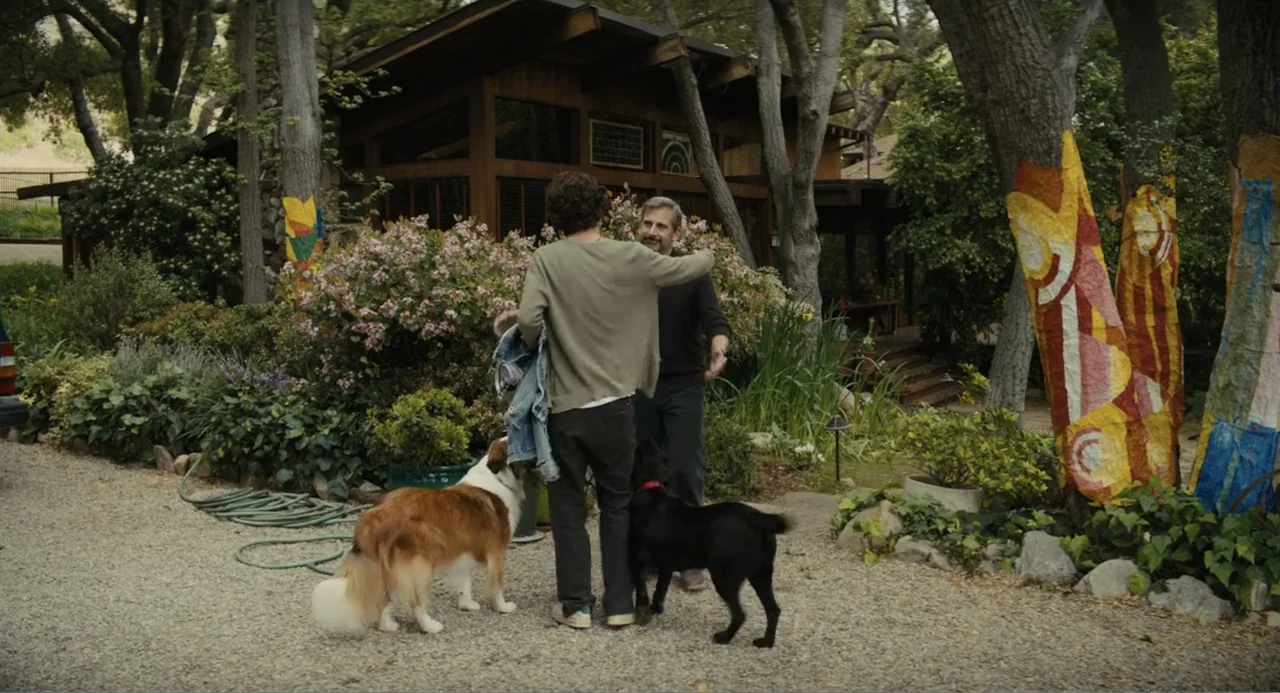 Beautiful Boy (2011) movie still: fullbody — A gravel driveway fronts a rustic wood-sided house nestled among trees and floral landscaping. Two men…
