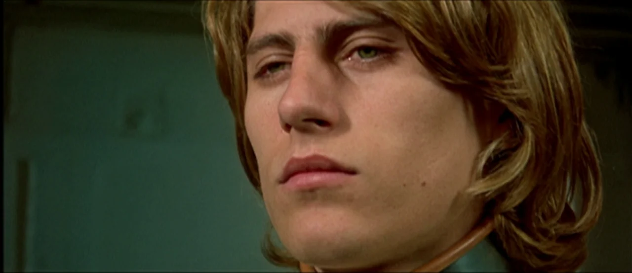 Flesh For Frankenstein (1973) movie still: closeup — A close portrait of a man in an indoor setting with dark walls. He maintains a steady gaze…