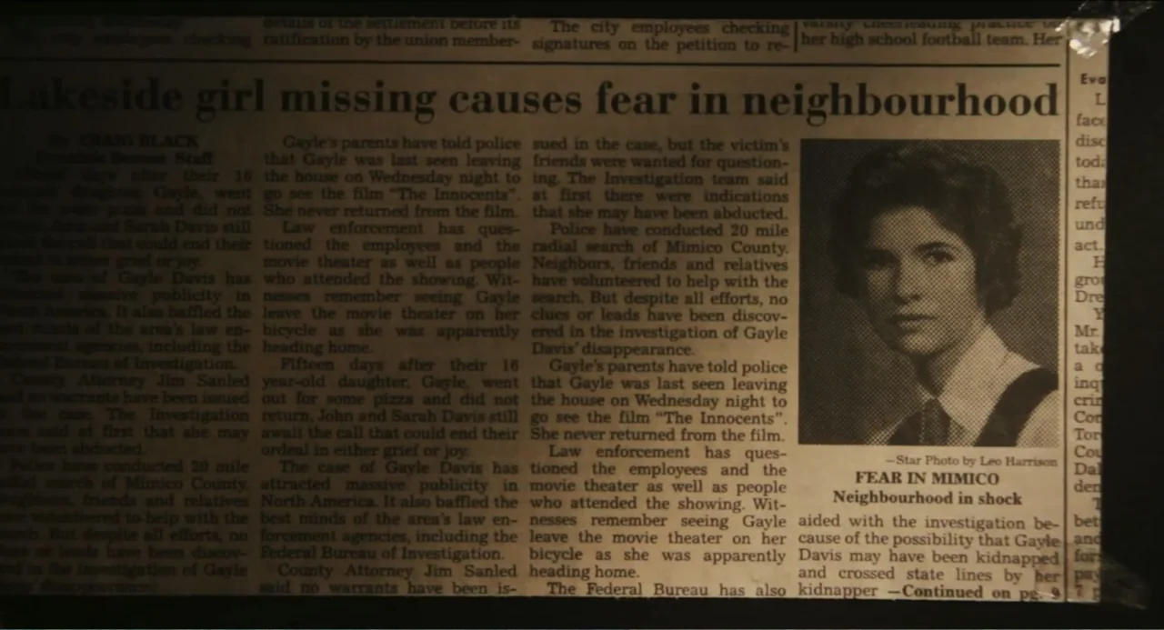 Haunter (2013) movie still: closeup — A newspaper page featuring a headline about a missing girl is lit in the dark. The text includes columns of…