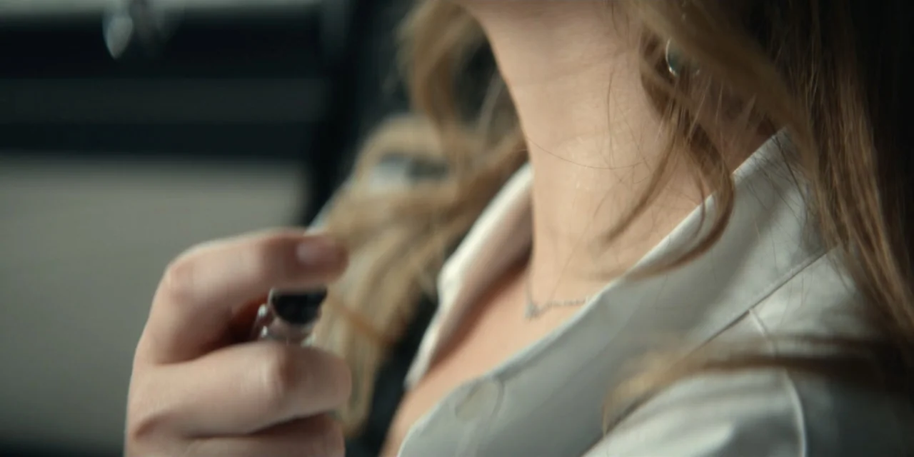 Our Fault (2025) movie still: closeup — A close view of a person's neck and shoulder inside a vehicle cabin. A hand holds a small glass spray bottle…