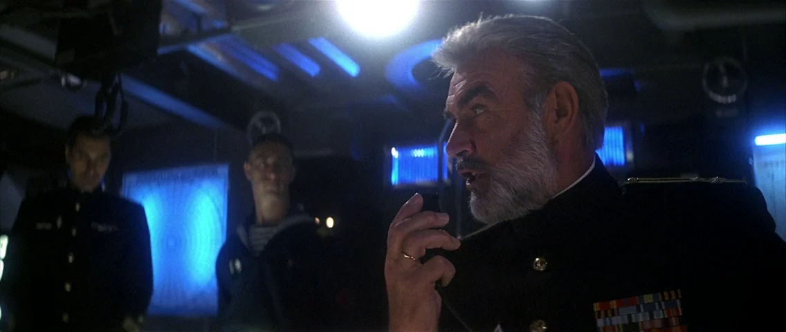 The Hunt for Red October (1990) movie still: medium — A cramped and dark naval control room with metallic equipment and glowing displays. An elderly…