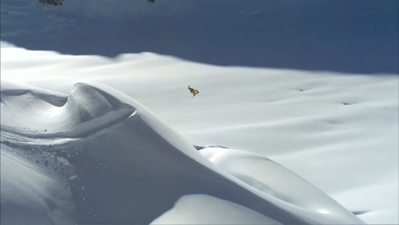Dear Rider: The Jake Burton Story (2021) movie still: wide — A vast, pristine snowy mountainside features large, wind-sculpted white drifts under a…