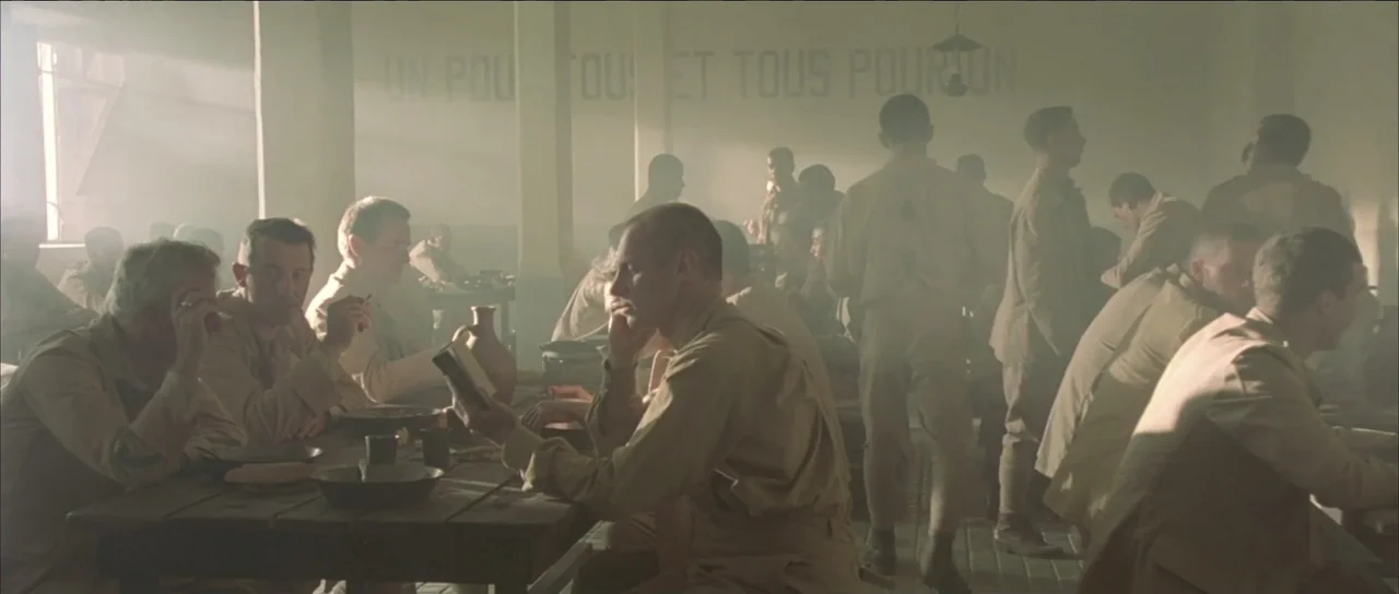 Legionario (2025) movie still: wide — A spacious military mess hall contains rows of long wooden tables occupied by soldiers. The room is filled…