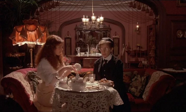 Yentl (1983) movie still: medium — A dimly lit parlor features dark red walls, decorative tassels, and a velvet sofa. A young woman and an older…