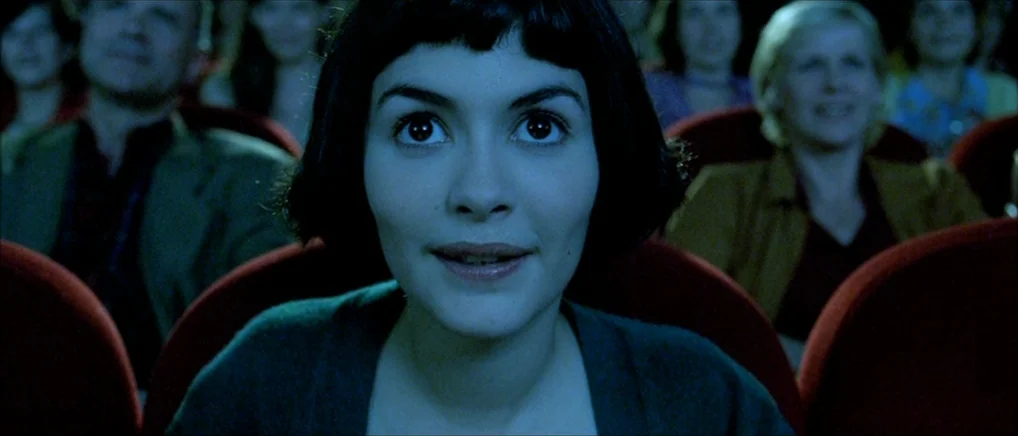 Amelie (2001) movie still: closeup — A dark movie theater auditorium with rows of red velvet seats behind the subject. A young woman with a dark bob…